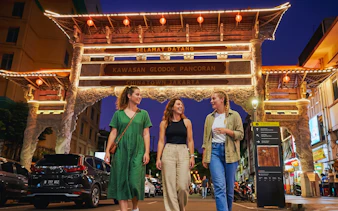 Three people walking under the illuminated Chinatown gate in Glodok, Jakarta at night.