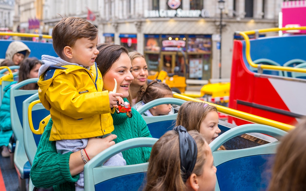 Children and adults on an open-top bus tour in London, enjoying city landmarks.