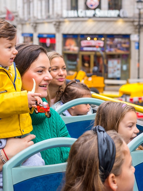 Children and adults on an open-top bus tour in London, enjoying city landmarks.