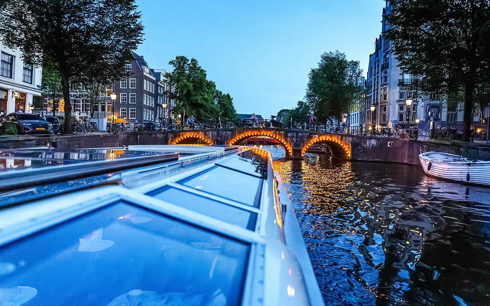 Canal cruise at dusk with illuminated bridge in Amsterdam.