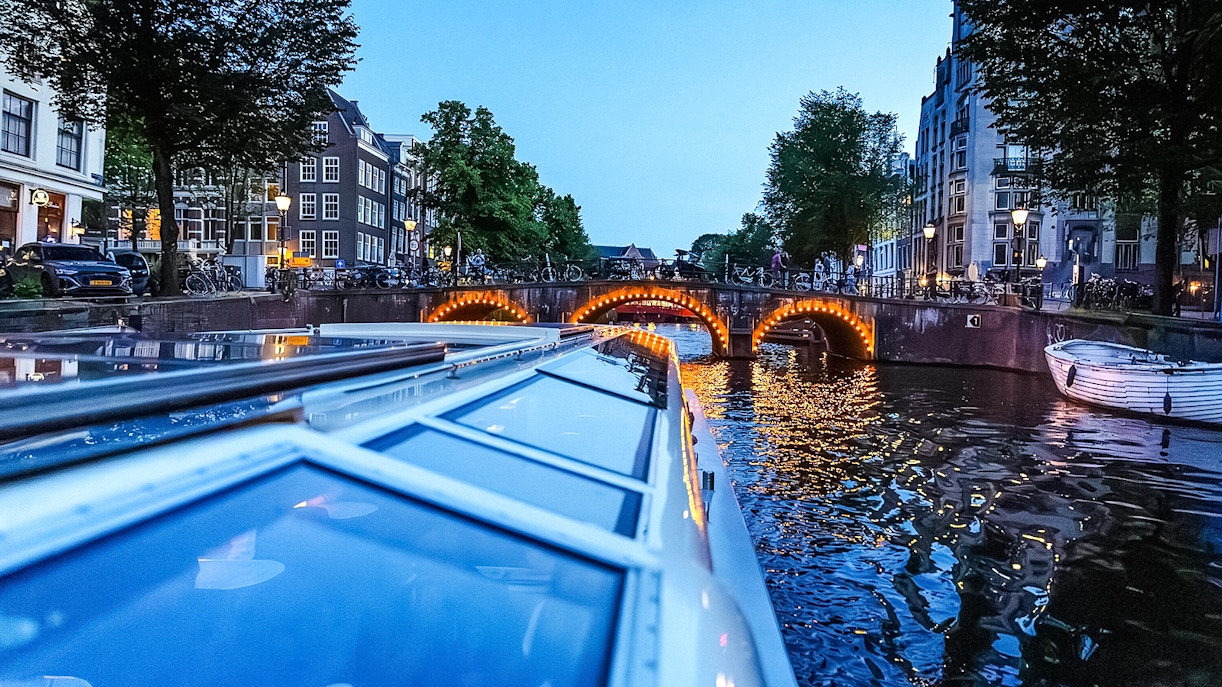 Canal cruise at dusk with illuminated bridge in Amsterdam.
