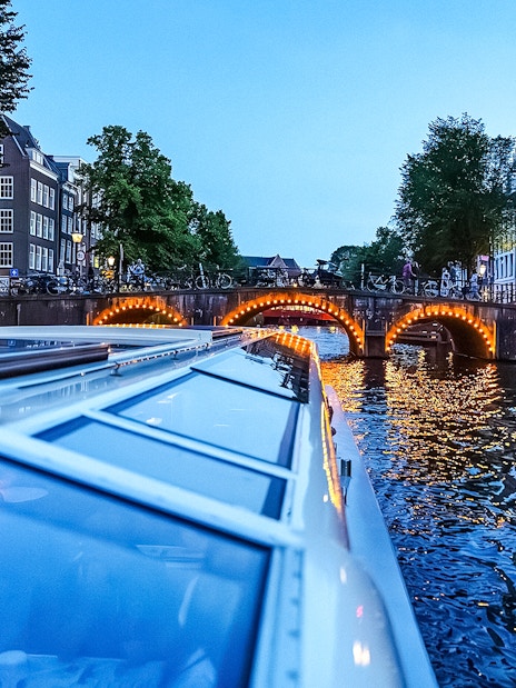 Canal cruise at dusk with illuminated bridge in Amsterdam.