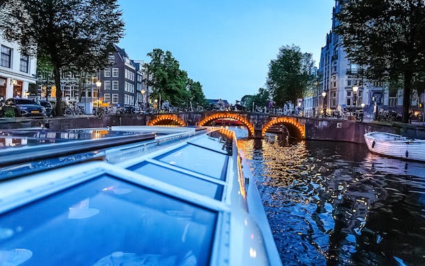 Canal cruise at dusk with illuminated bridge in Amsterdam.