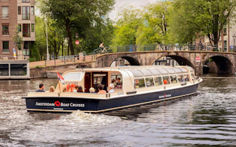 Guests enjoying Amsterdam Canal Cruise with FEBO snacks, passing under a historic bridge.