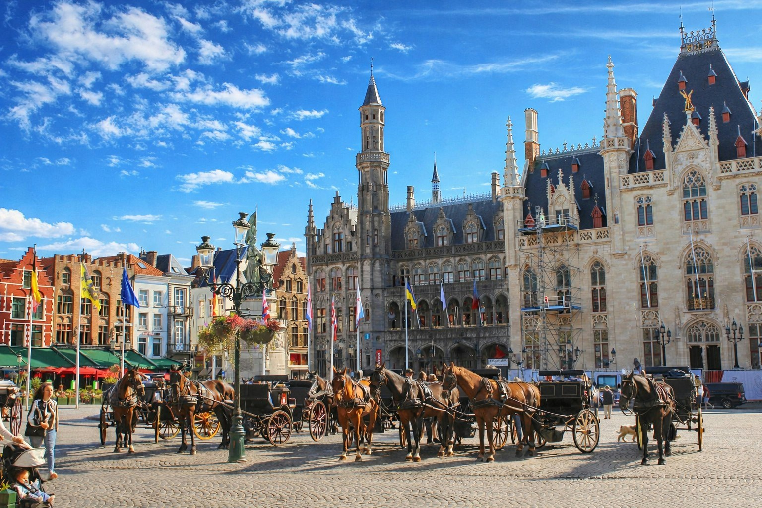 Horse-drawn carriages in Burg Square, Bruges, Belgium, with medieval buildings in the background.