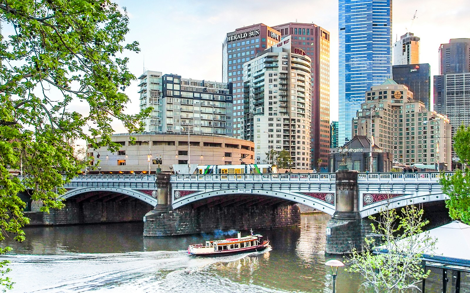 Boat cruising under Princes Bridge on Yarra River, Melbourne cityscape in background.