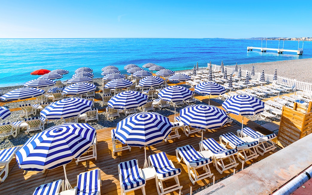 Striped umbrellas and sun loungers on a beach in St Tropez, part of the Nice to Port Grimaud day tour.