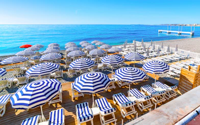Striped umbrellas and sun loungers on a beach in St Tropez, part of the Nice to Port Grimaud day tour.