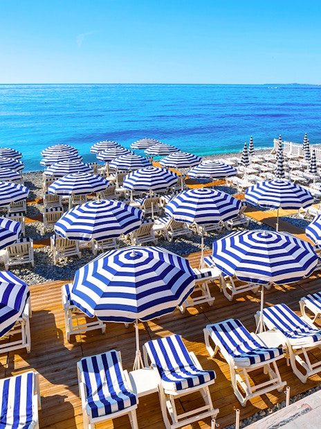 Striped umbrellas and sun loungers on a beach in St Tropez, part of the Nice to Port Grimaud day tour.