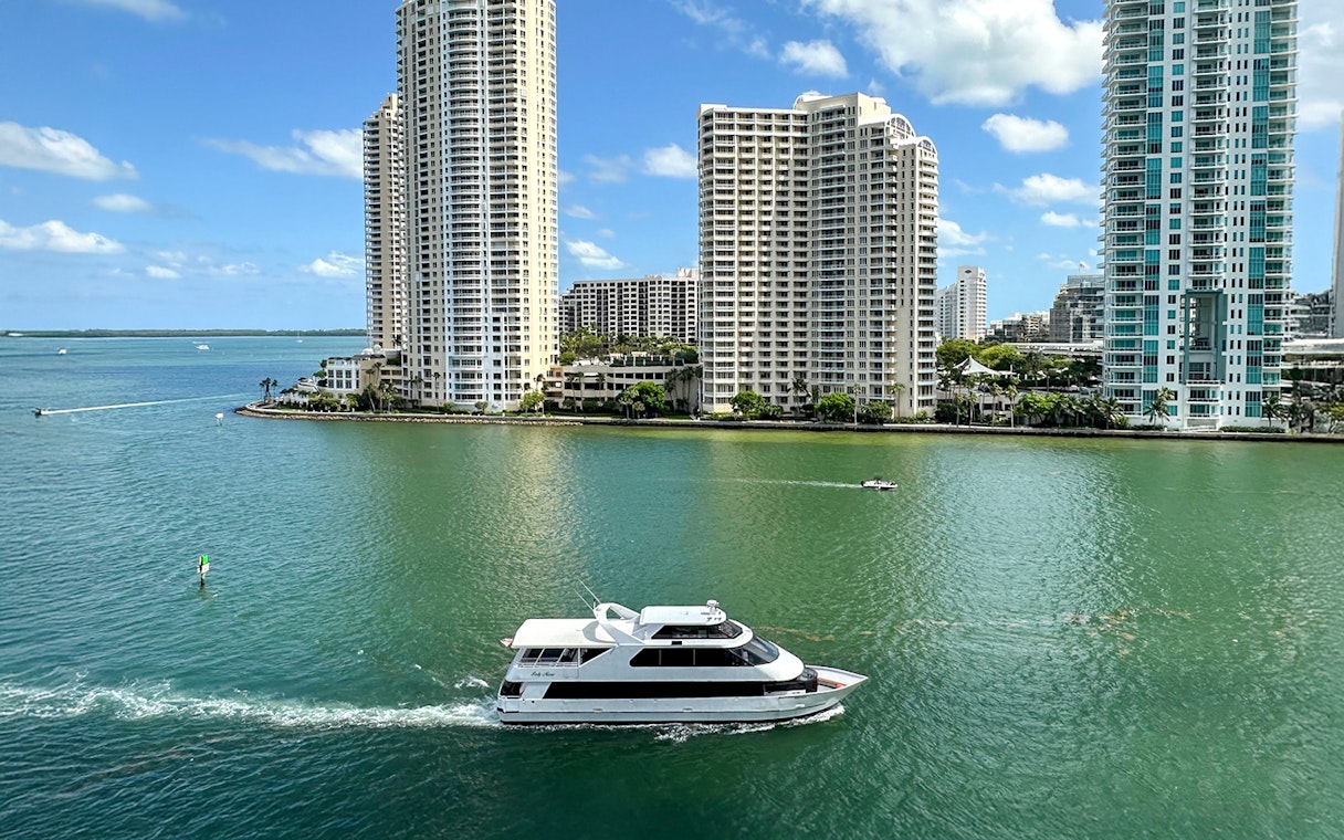 Luxury yacht cruising past Miami skyline with high-rise buildings.