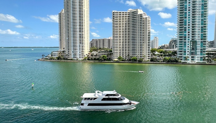 Luxury yacht cruising past Miami skyline with high-rise buildings.