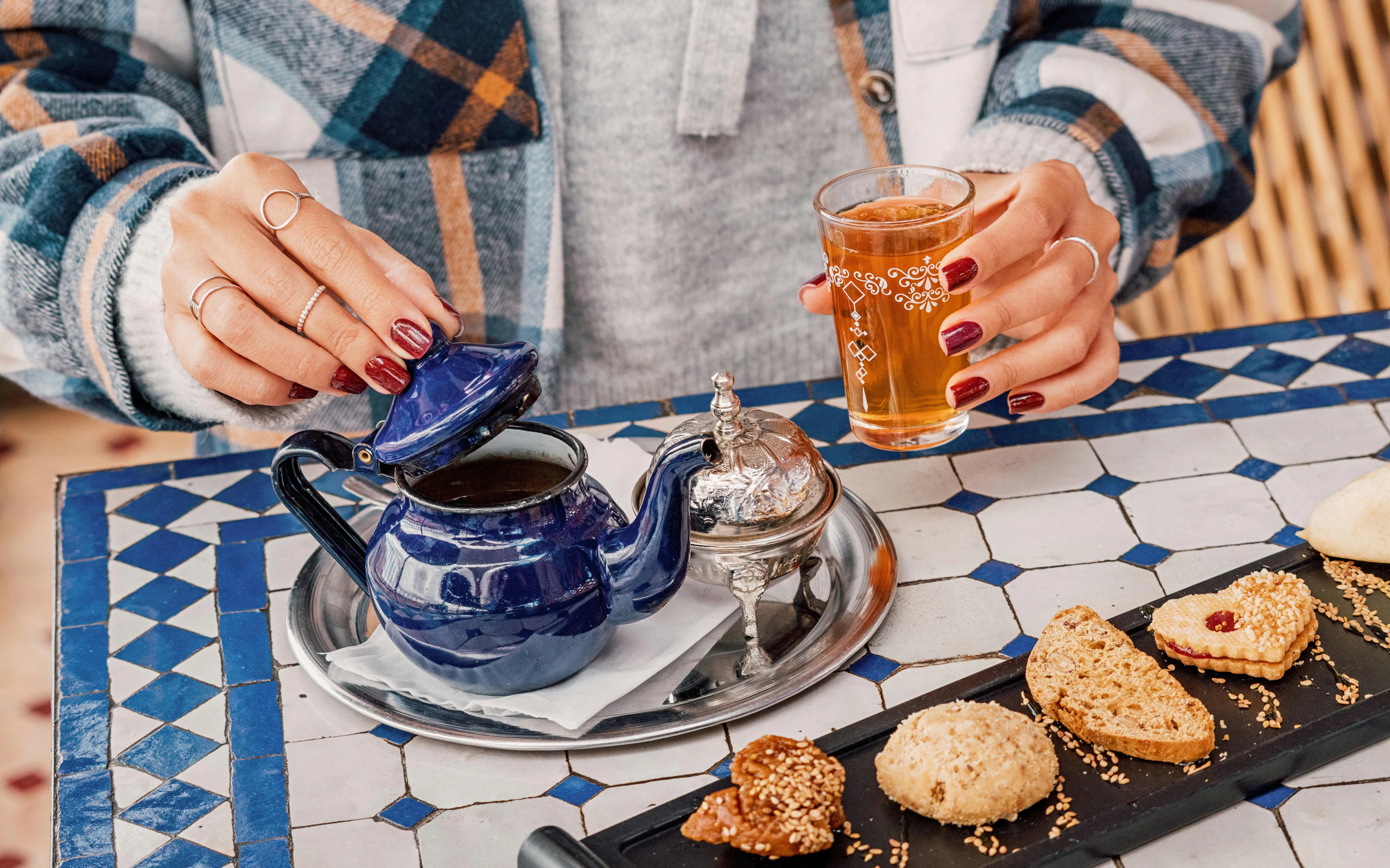 Woman pouring tea from a blue teapot, enjoying Moroccan pastries in a riad courtyard.