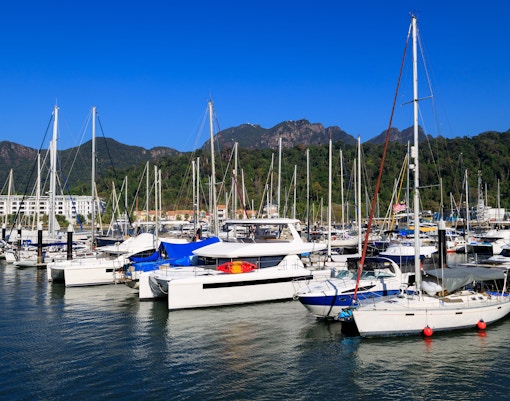 Boats docked at Telaga Harbor in Langkawi with lush green hills in the background.