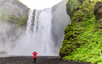 Visitors viewing Skogafoss waterfall in Iceland with lush green cliffs.