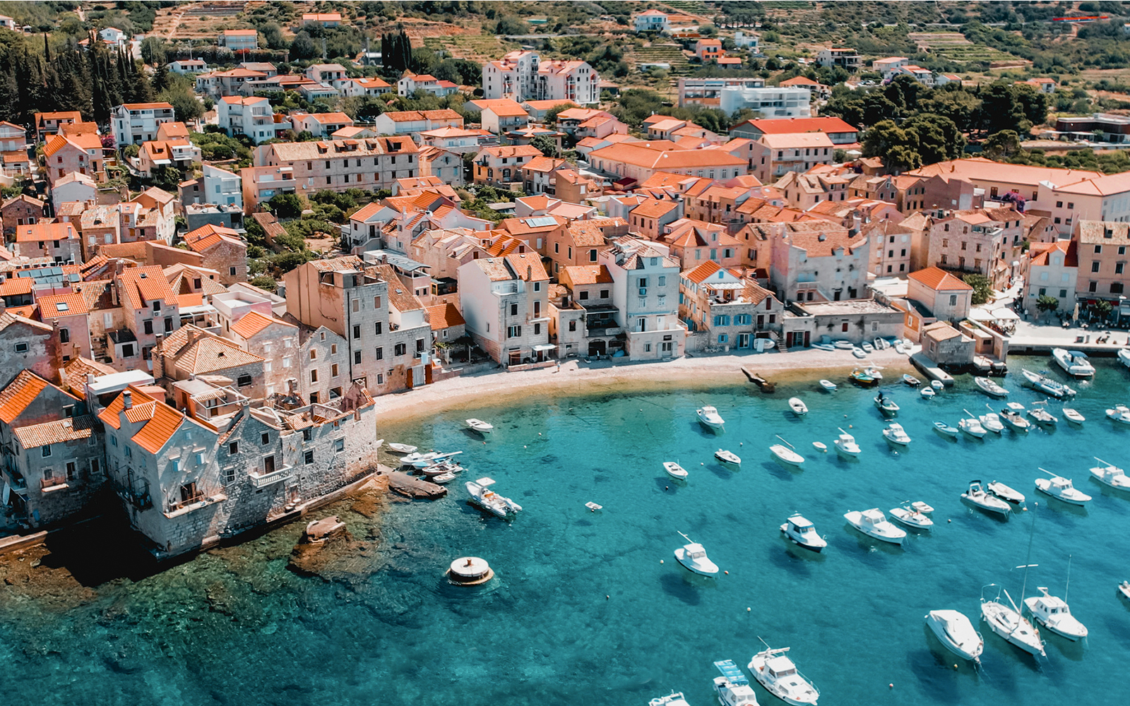 Aerial view of Hvar island's coastal town with boats in turquoise water.
