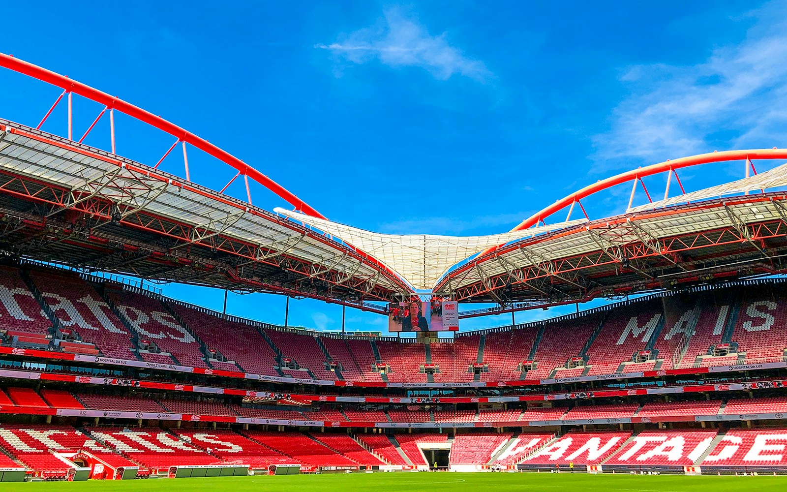 Benfica Stadium ground view with red seating and arched roof structure.