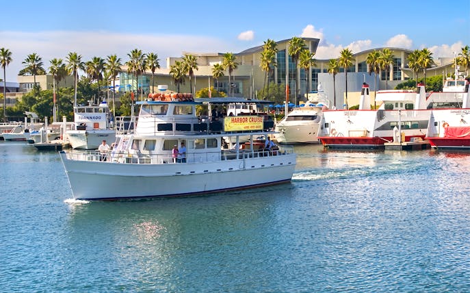 Cruise boat navigating Los Angeles Harbor with palm trees and buildings in the background.