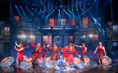 Performers dancing with umbrellas on a water-filled stage at WOW: The Vegas Spectacular.