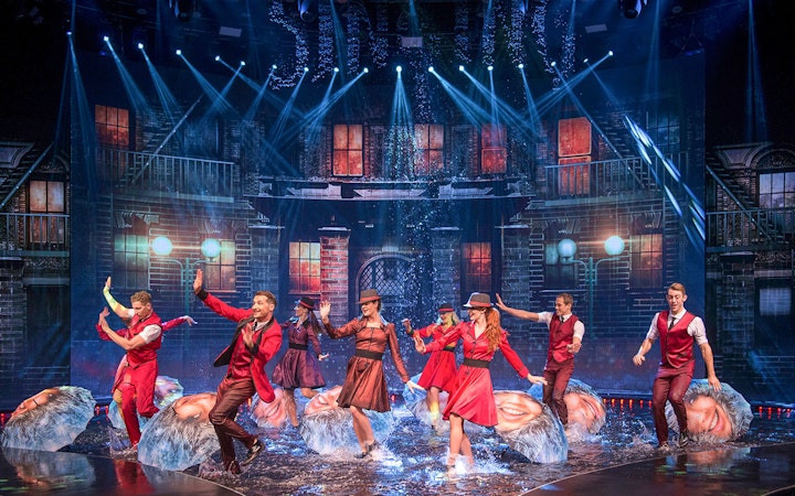 Performers dancing with umbrellas on a water-filled stage at WOW: The Vegas Spectacular.