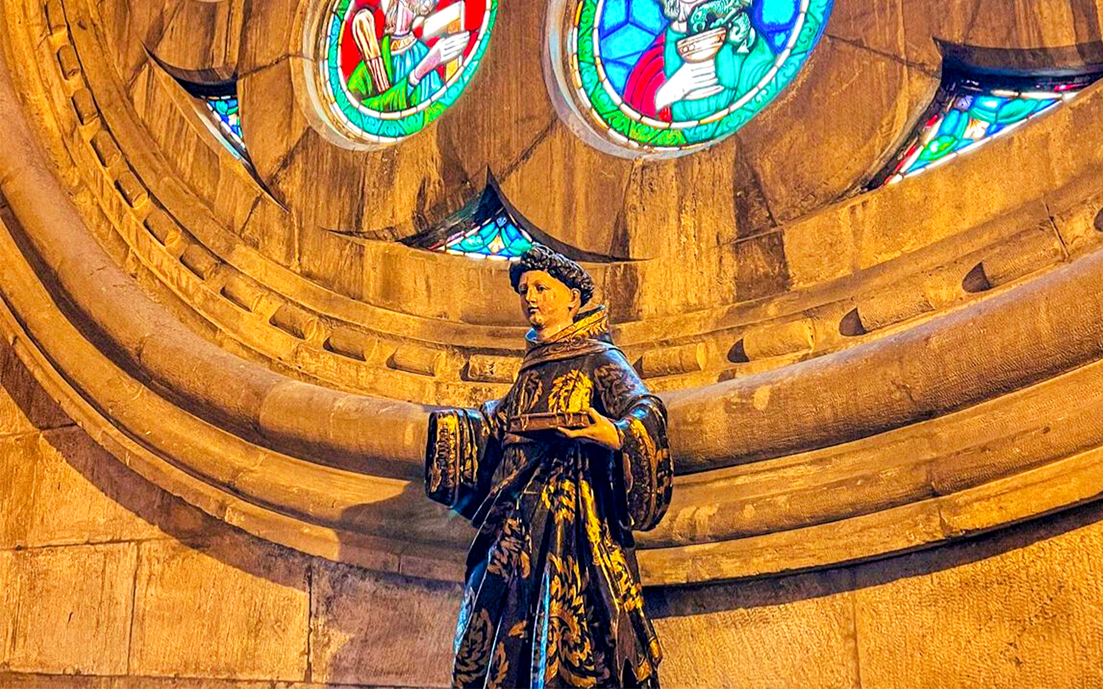Statue inside church with stained glass windows above.