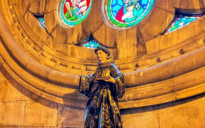 Statue inside church with stained glass windows above.