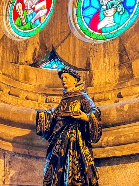 Statue inside church with stained glass windows above.