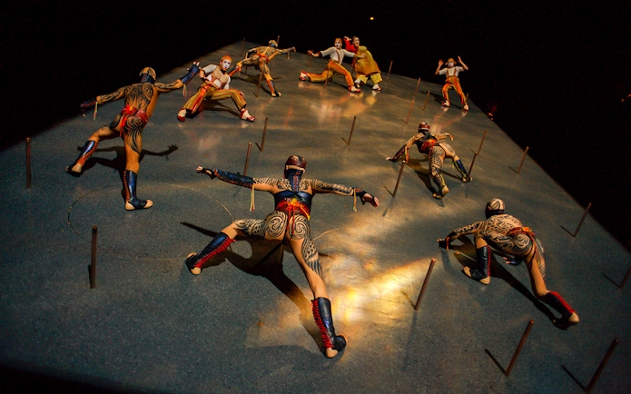 Performers in intricate costumes climbing a vertical stage in Cirque du Soleil KÀ show.