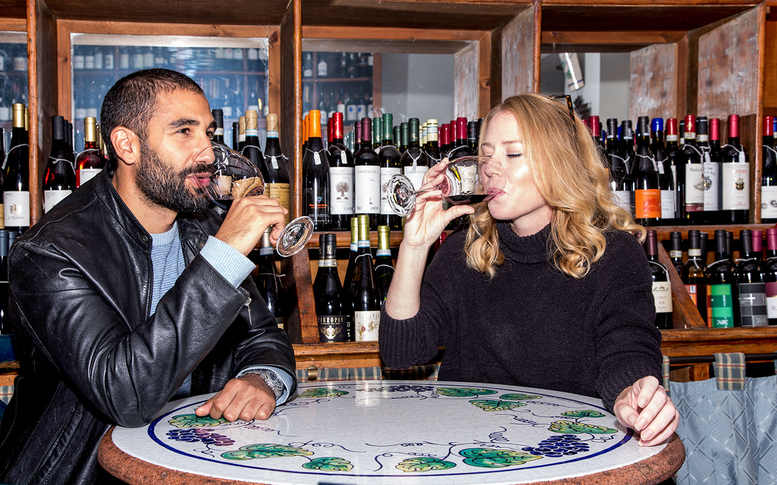 Friends enjoying wine at a bar with bottles displayed in the background.