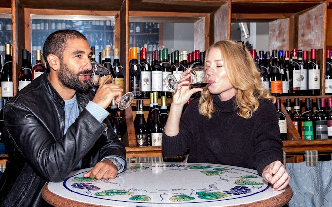 Friends enjoying wine at a bar with bottles displayed in the background.