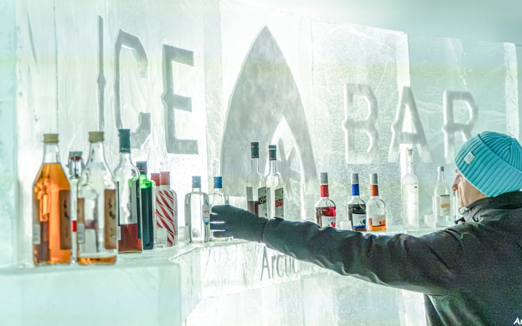 Guest reaching for a bottle at the ice bar inside Arctic SnowHotel.