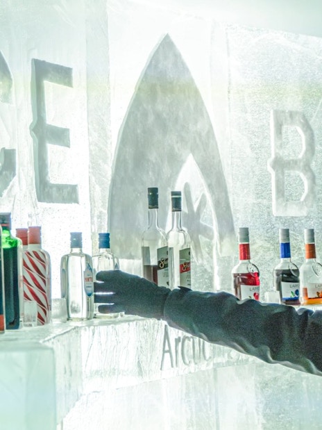 Guest reaching for a bottle at the ice bar inside Arctic SnowHotel.
