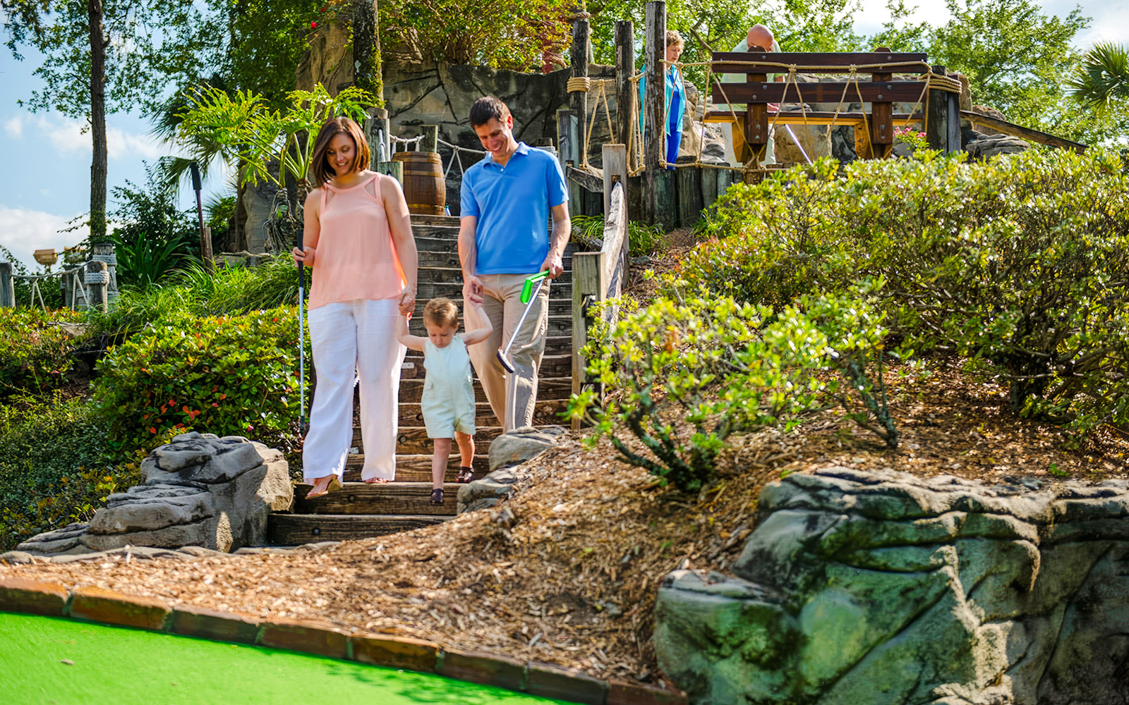 Family walking down steps at Pirate's Cove Adventure Golf, surrounded by lush greenery and rock formations.