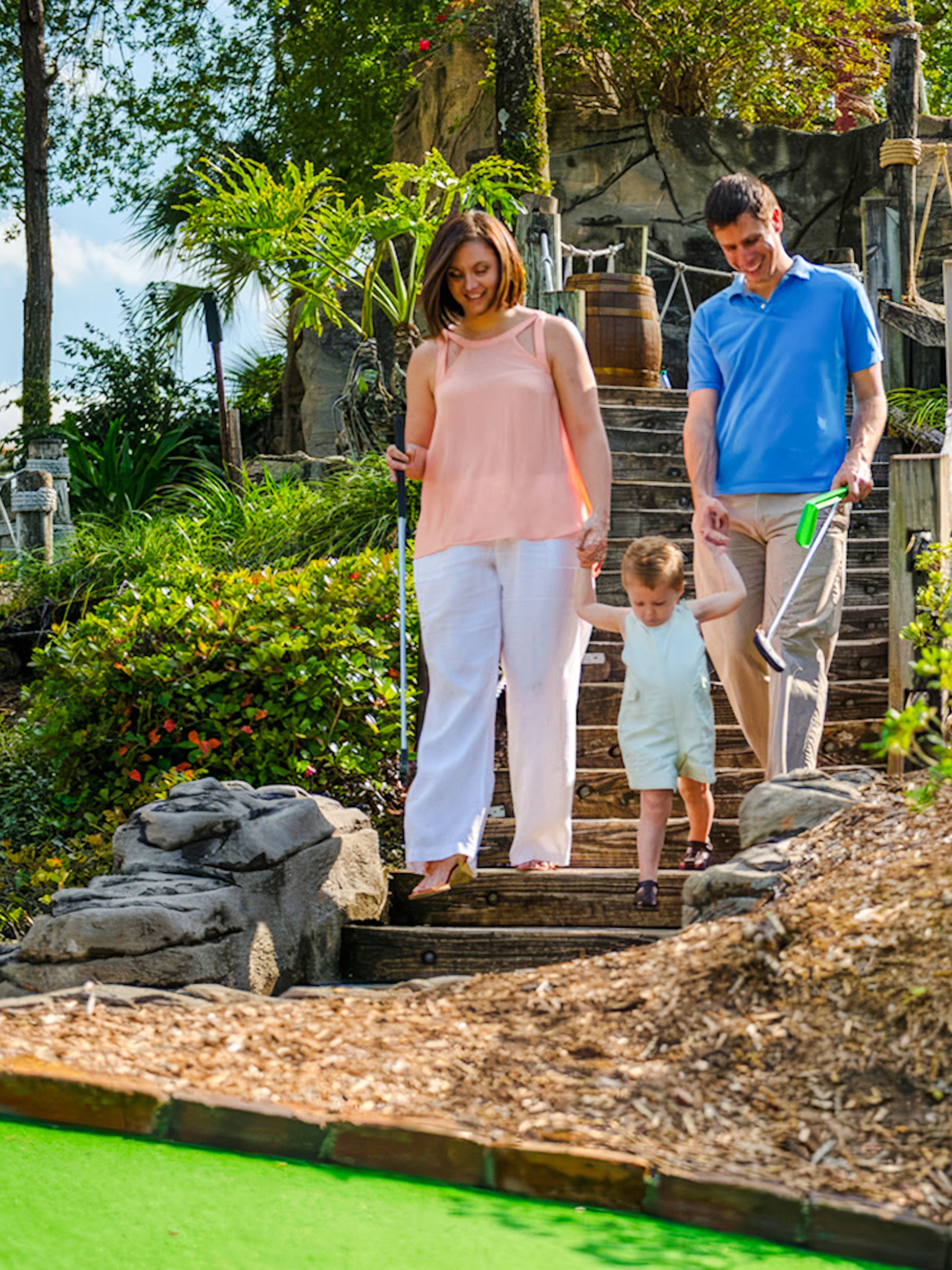 Family walking down steps at Pirate's Cove Adventure Golf, surrounded by lush greenery and rock formations.