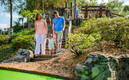 Family walking down steps at Pirate's Cove Adventure Golf, surrounded by lush greenery and rock formations.