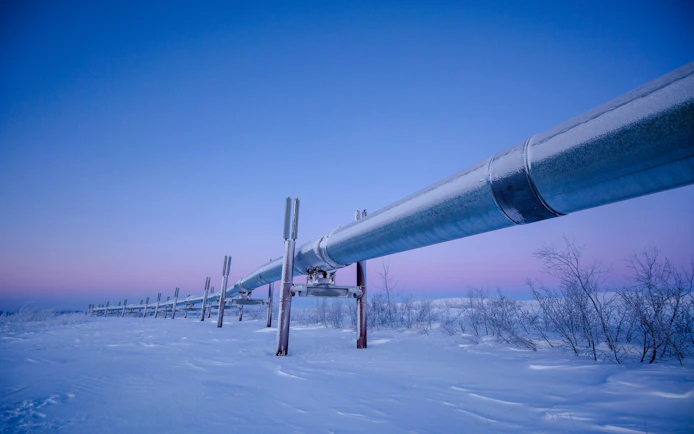 Dalton Highway oil pipeline in snowy landscape at dusk.