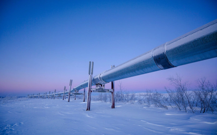 Dalton Highway oil pipeline in snowy landscape at dusk.