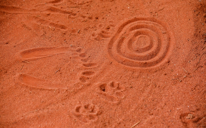 Aboriginal sand art and footprints at Uluru during sunrise tour.