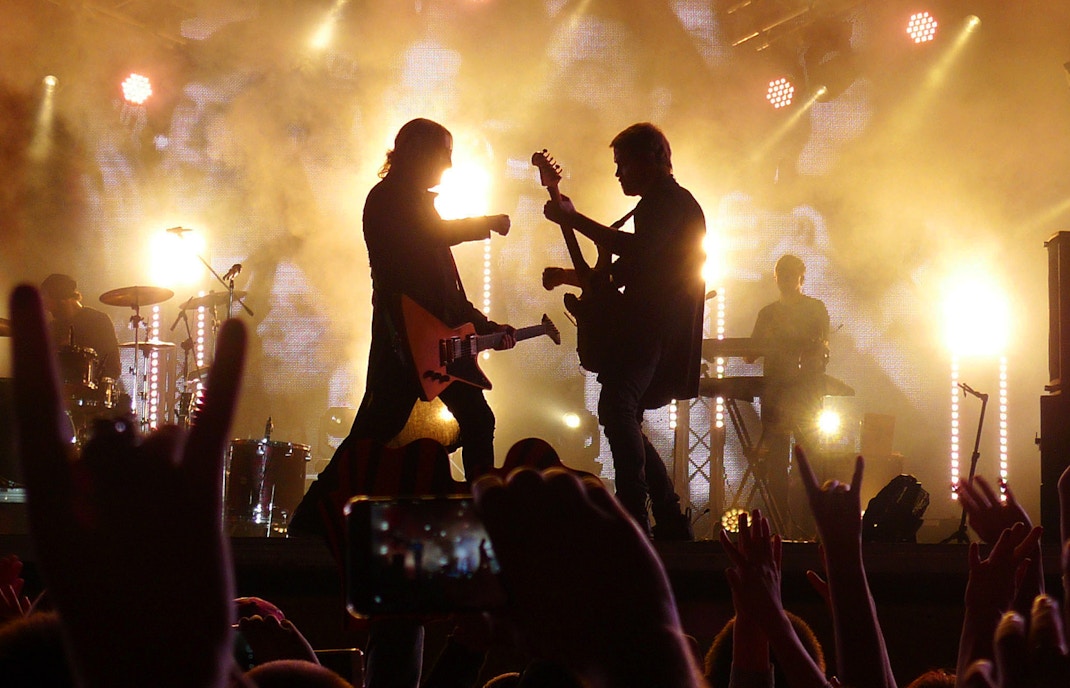 Silhouettes of guitarists performing on stage with bright lights at a concert.