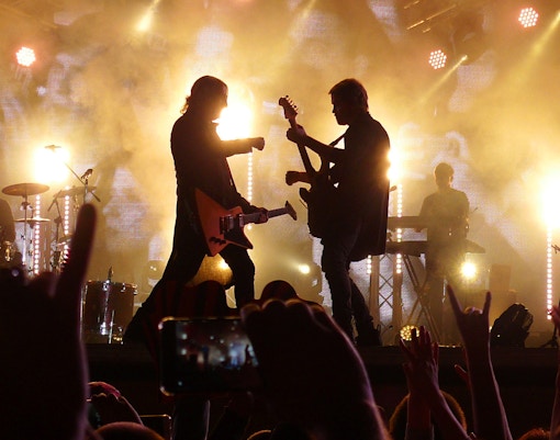 Silhouette of guitarists performing on stage with bright lights at a concert.