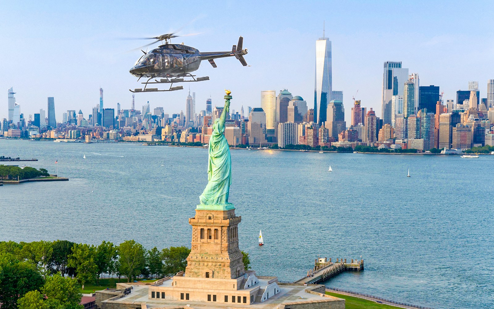 Helicopter flying over Statue of Liberty with New York City skyline in background.