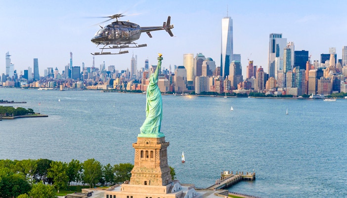Helicopter flying over Statue of Liberty with New York City skyline in background.