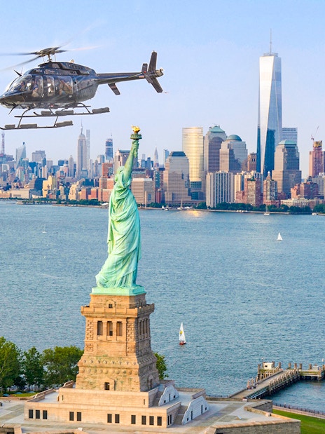 Helicopter flying over Statue of Liberty with New York City skyline in background.