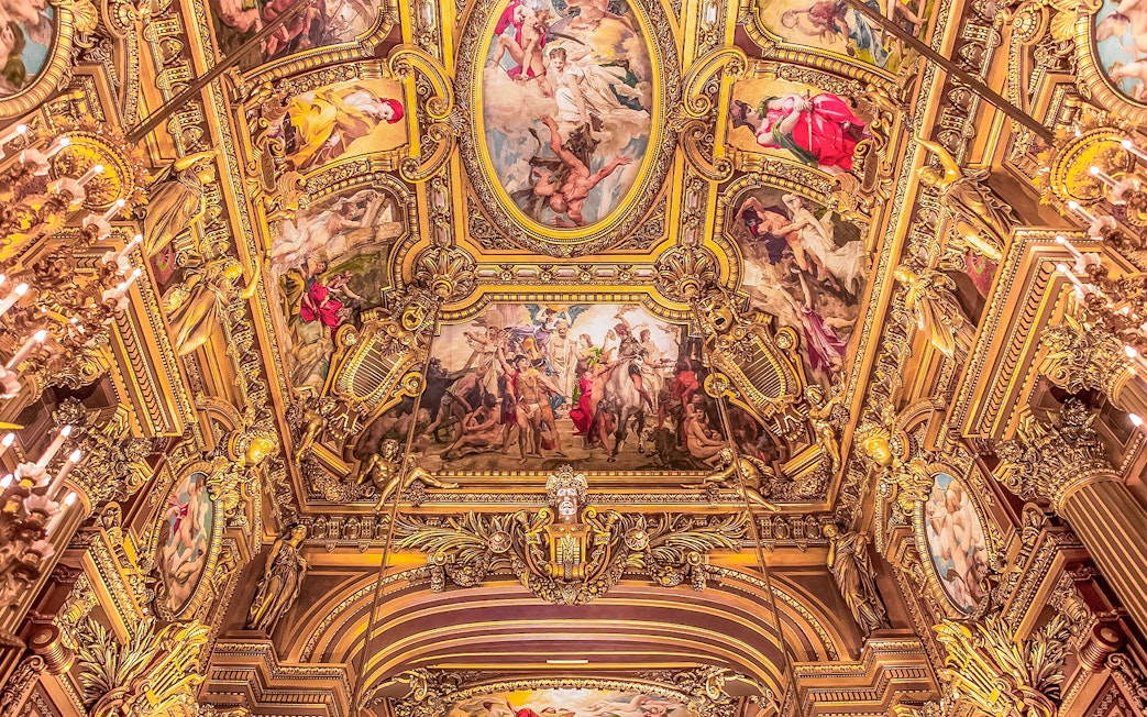 Ornate ceiling frescoes at Opera Garnier, Paris, featuring classical figures and gold detailing.