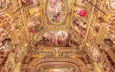Ornate ceiling frescoes at Opera Garnier, Paris, featuring classical figures and gold detailing.