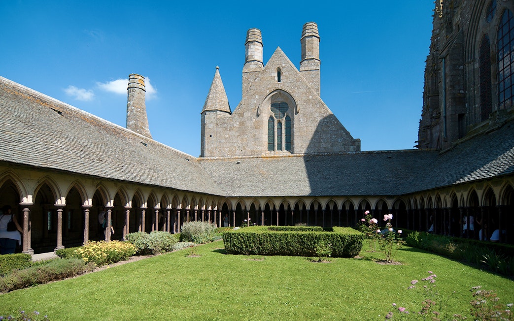 Cloister garden at Mont Saint Michel Abbey, France, under a clear blue sky.