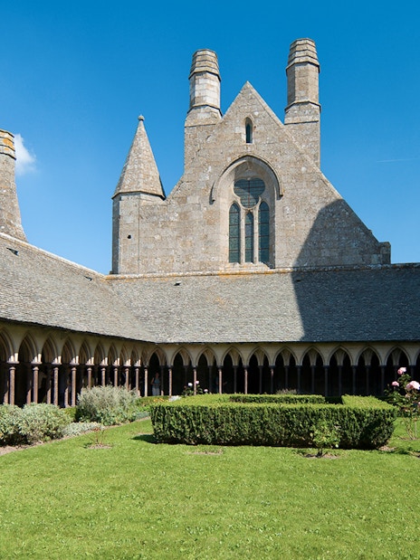 Cloister garden at Mont Saint Michel Abbey, France, under a clear blue sky.