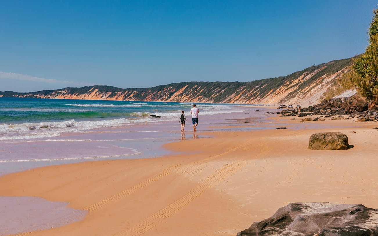 Beach view with people walking along the shore, part of the 6-hour kayak and 4WD tour from Noosa.