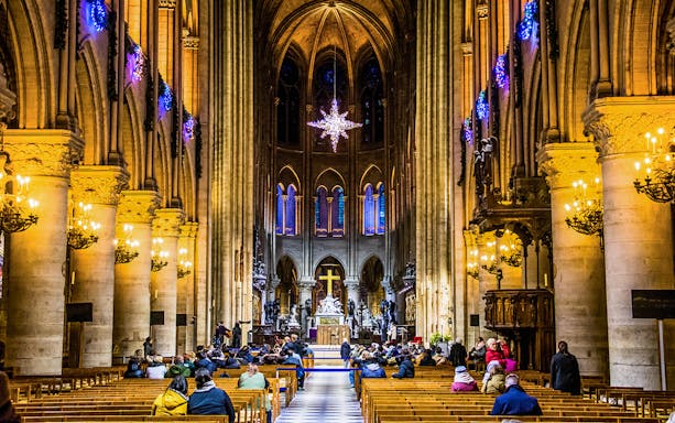Interior of Notre Dame Cathedral with visitors seated, Paris.