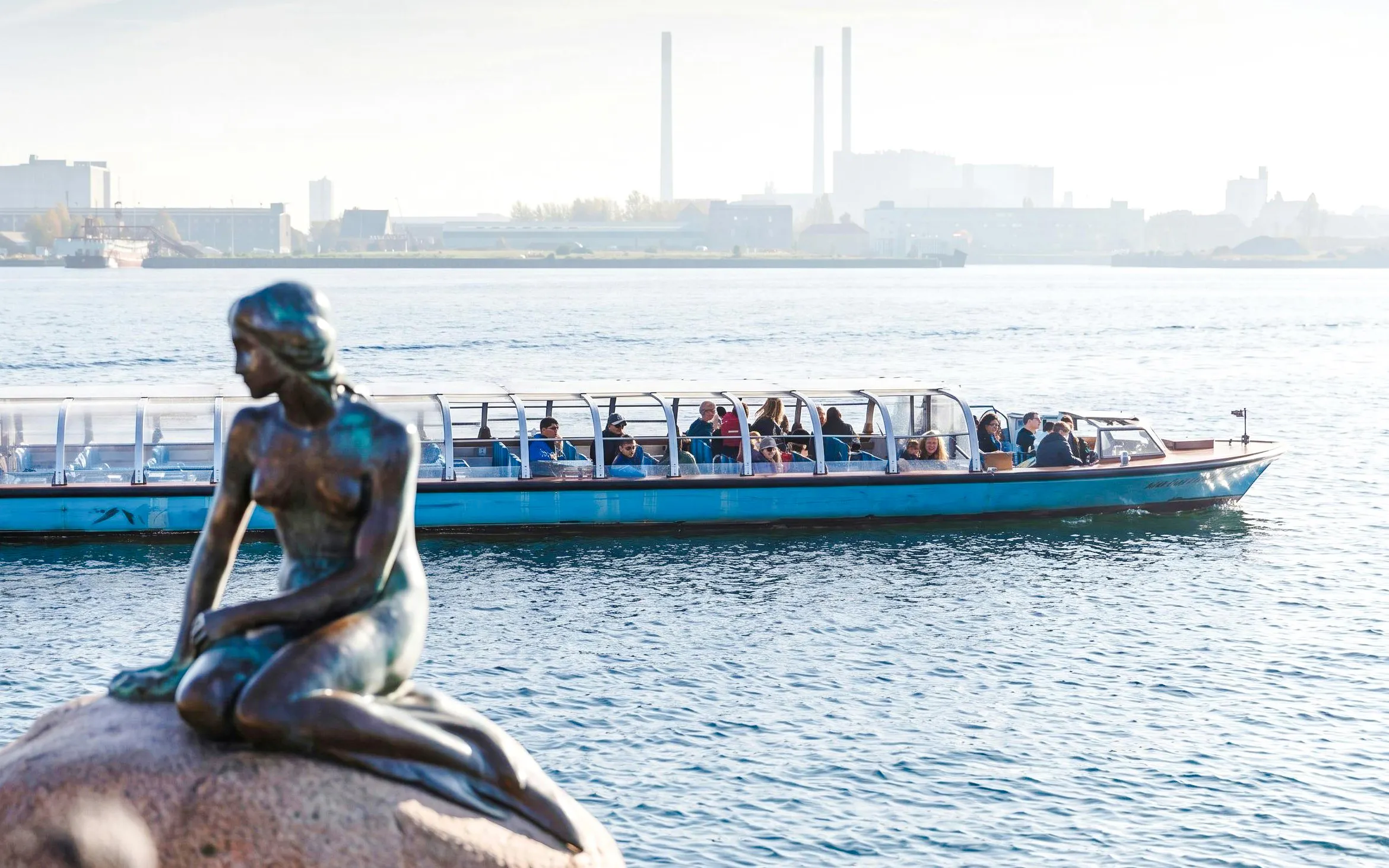 Red Sightseeing Netto boat passing by the Little Mermaid statue in Copenhagen.