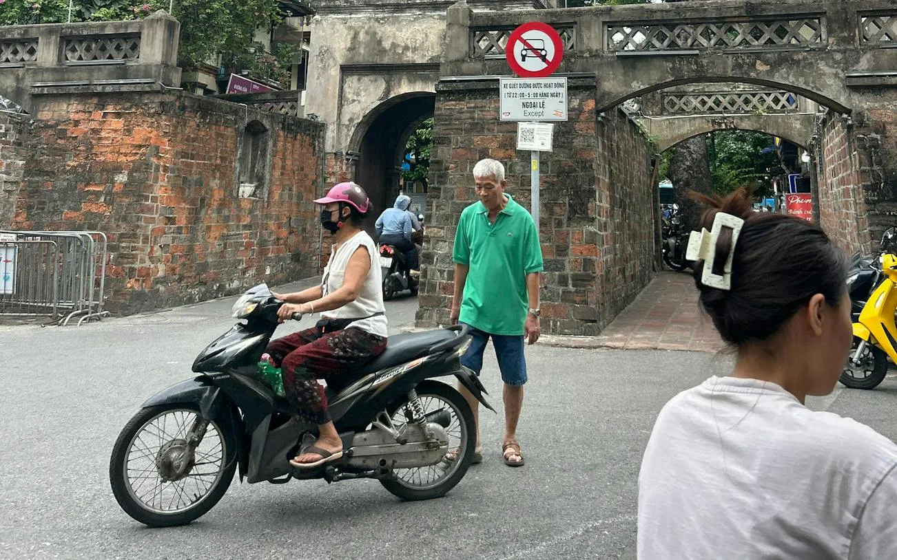 Scooter and pedestrian near ancient gate in Hanoi Old Quarter.
